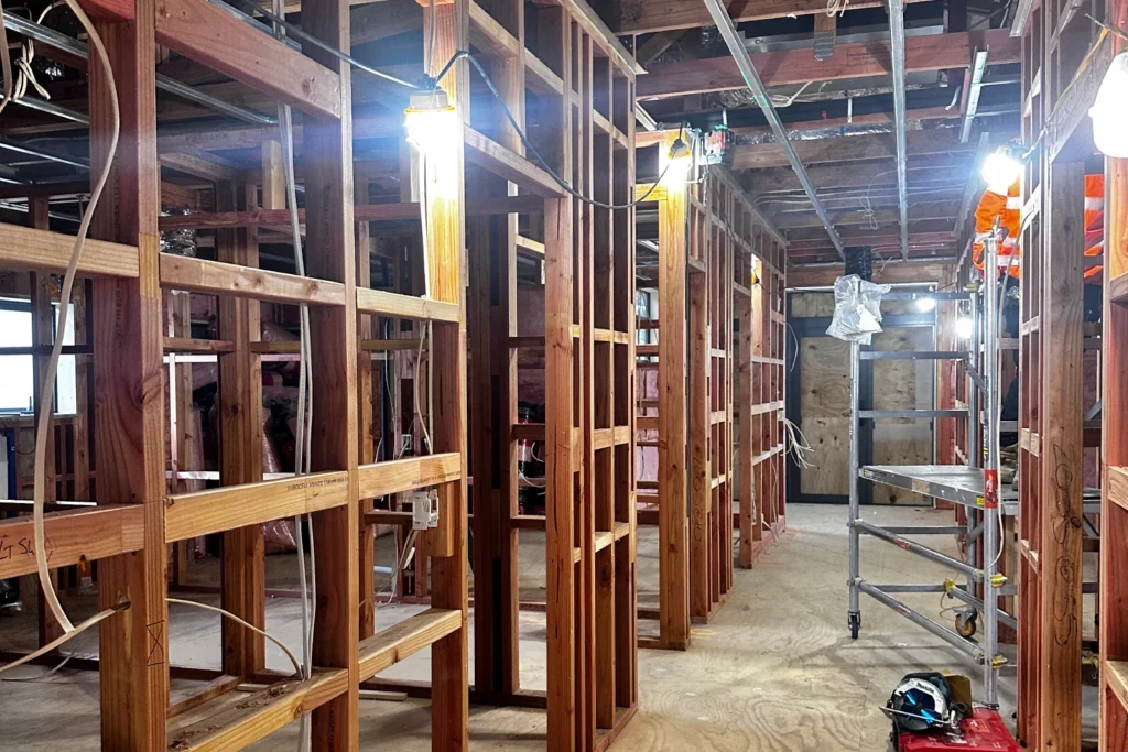 Interior of the existing building stripped back to framing, lit by temporary work lights, with a mobile scaffold tower in place